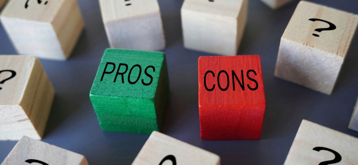 Wooden blocks with "PROS" and "CONS" written on them in black letters, the "PROS" block is green and the "CONS" block is red. Surrounding these blocks are other wooden blocks with black question marks on them. The image conveys a concept of weighing pros and cons amidst uncertainty such as when comparing different types of pool heating systems.