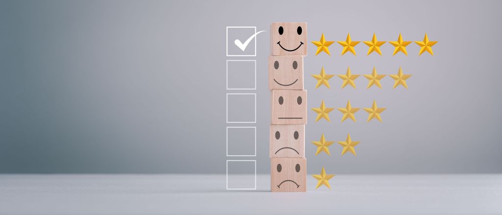 A stack of wooden blocks displaying different facial expressions, from top to bottom: a smiling face with five gold stars, a neutral face with four gold stars, a slightly sad face with three gold stars, and a very sad face with one gold star. To the left of the stack is a vertical row of empty checkboxes, with the topmost box checked. The image represents a rating or feedback system. This is symbolic of the Heliocol Solar Pool Heating System being the top choice for our customers.