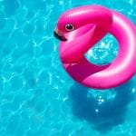 Bright pink inflatable pool float in the shape of a flamingo, floating on the surface of a clear, blue swimming pool with sunlight reflecting off the water.