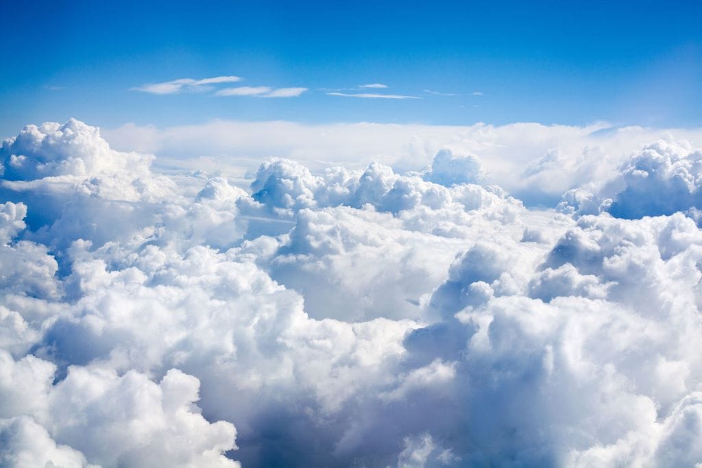 A scenic aerial view of thick, fluffy white clouds stretching across the sky under a clear blue atmosphere, capturing the serene and expansive beauty above the clouds.