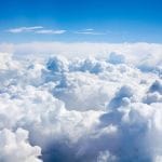 A scenic aerial view of thick, fluffy white clouds stretching across the sky under a clear blue atmosphere, capturing the serene and expansive beauty above the clouds.