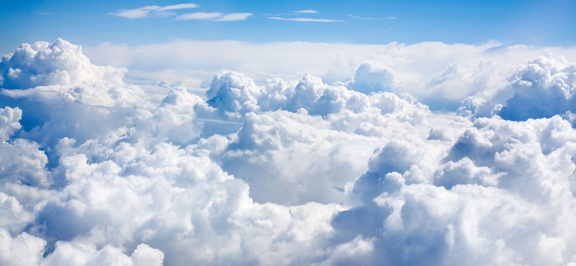 A scenic aerial view of thick, fluffy white clouds stretching across the sky under a clear blue atmosphere, capturing the serene and expansive beauty above the clouds.