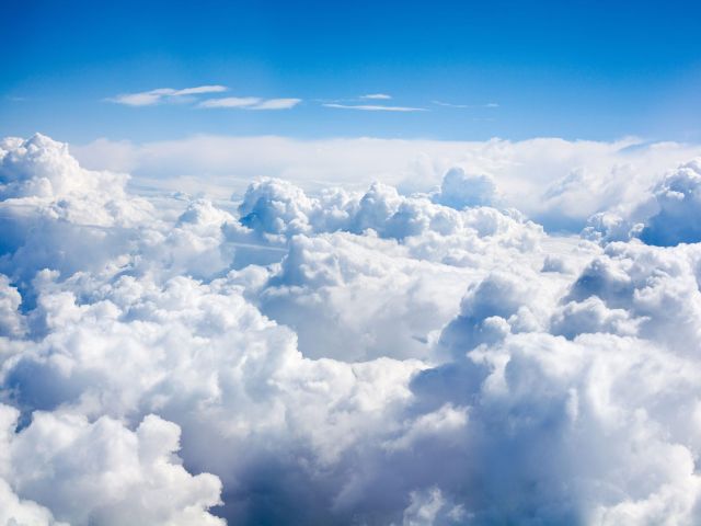 A scenic aerial view of thick, fluffy white clouds stretching across the sky under a clear blue atmosphere, capturing the serene and expansive beauty above the clouds.