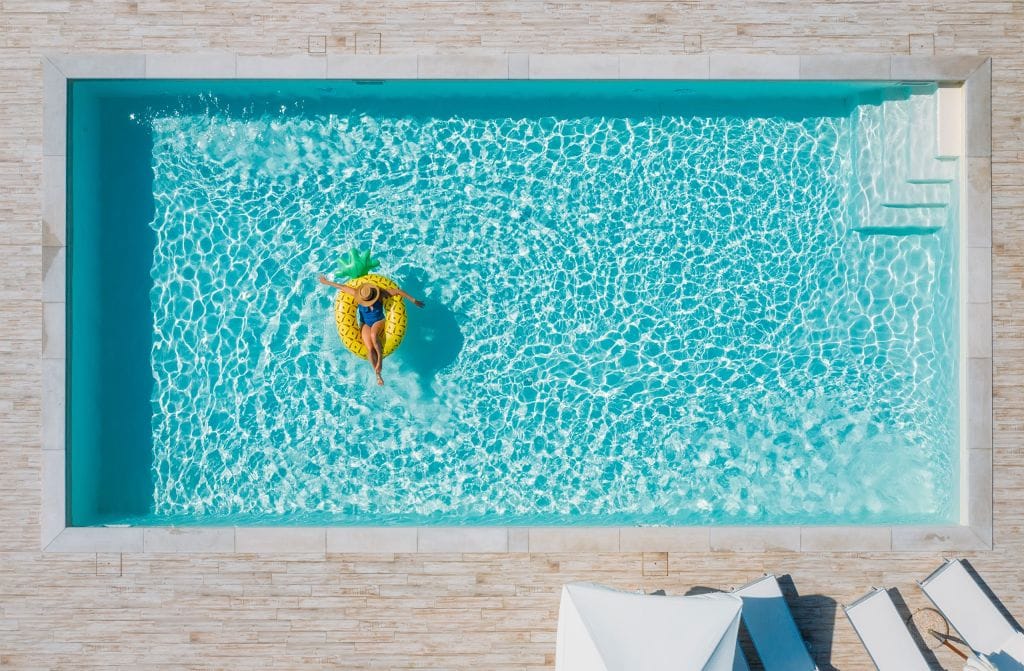Person floating on a pineapple-shaped inflatable in a bright blue swimming pool, viewed from above.