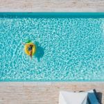 Person floating on a pineapple-shaped inflatable in a bright blue swimming pool, viewed from above.